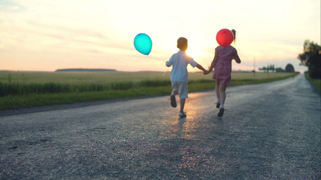 Young children run hopping on road sunset with balloons