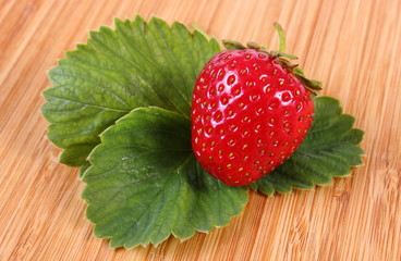 Strawberry with leaves on wooden surface