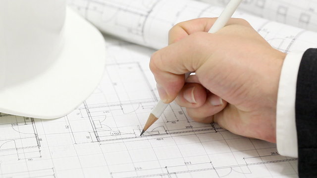 Male architect checking numbers on blueprint during house construction planing
