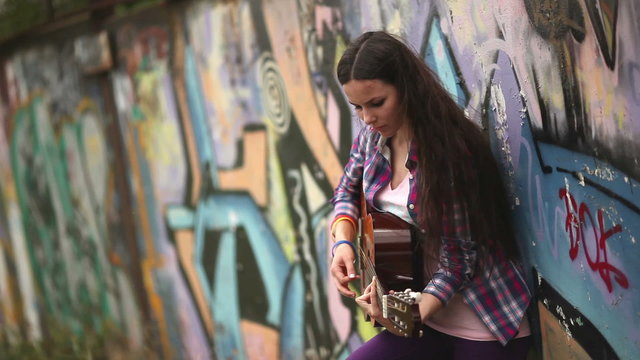 Девушка играет на гитаре опираясь на стену с граффити