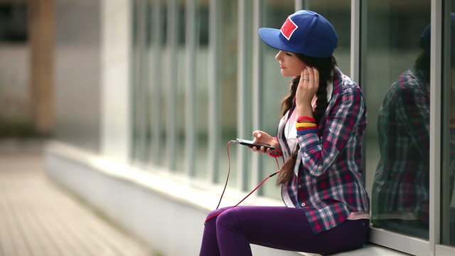 Девушка в кепке слушает музыку на телефоне