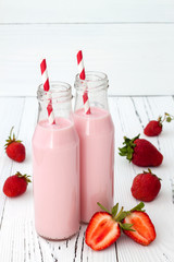 Strawberry milk in traditional glass bottles with straws on old vintage wooden background