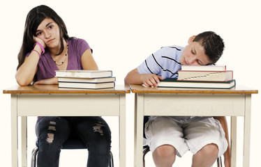 Studio shot on neutral background of two bored kids at their school desks.