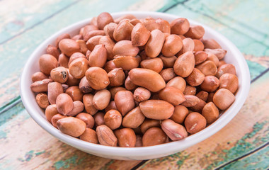 Ground nut or peanuts in white bowl over weathered wooden background