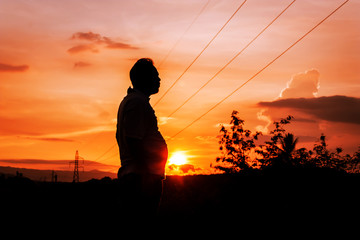 silhouette of man fat standing at sunset in the mountains and high voltage electricity pylon