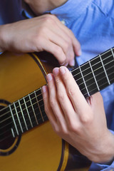 Obraz premium Acoustic guitar's fretboard and young male's hands