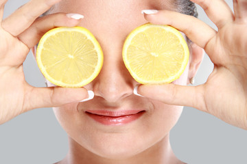 woman smiling while holding slices of lemon in front of her eyes