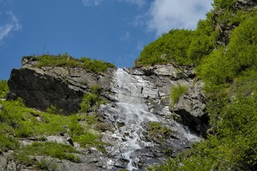 High waterfall in Carpathians mountains under blue sky.