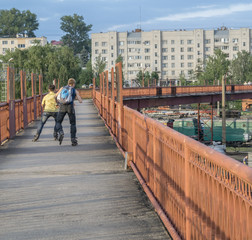 Two young boys riding on roller skates on a long wrap bridge ove