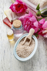Fototapeta na wymiar Bowl of sea salt, essential oils, bars of soap and peony flowers