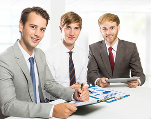 three businessmen smiling and looking at camera while meeting at