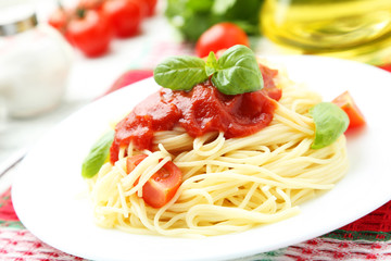 Spaghetti with tomatoes and basil on plate on white wooden backg