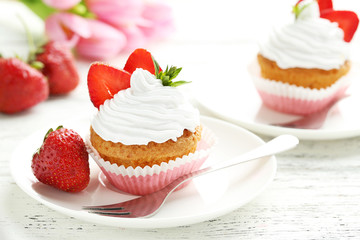 Tasty cupcake with fresh strawberry on white wooden background