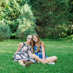 Two women of different generations sitting on the grass in the park. Mother and daughter. Grandmother and granddaughter.