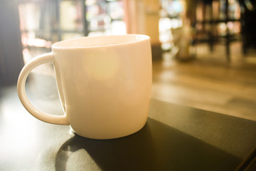 Close up a white cup of coffee on black table with blur background coffee shop - vintage filter and sun flare filter effect