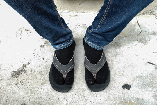 Close up man's lags in jeans with socks and slippers