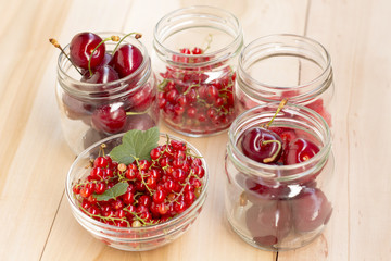 Fototapeta na wymiar Glass jars with different fruit (redcurrant, raspberry and cherries) on a wooden table 