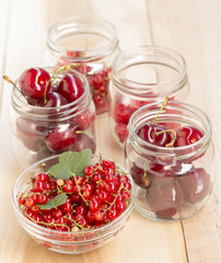 Glass jars with different fruit (redcurrant, raspberry and cherries) on a wooden table
