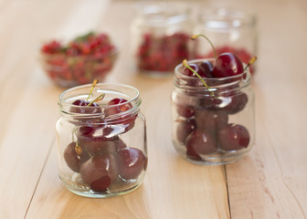 Glass jars with different fruit (redcurrant, raspberry and cherries) on a wooden table
