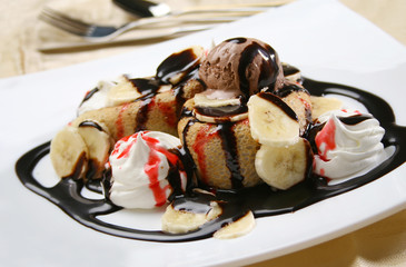 Rolled crepes with scoop of ice cream and chocolate topping on a plate, shallow depth of field