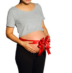 Belly of pregnant woman with red ribbon on white.
