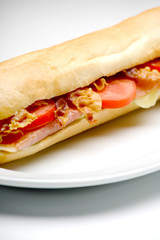 Sandwich with ham, bacon and tomato on a plate, close up studio shot, isolated on white, shallow depth of field