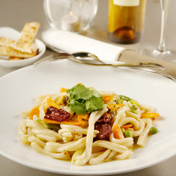 Dried tomato pasta served with white wine in background, close up shot