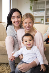 Obraz premium Female couple sit together with their son in their home and all smile for the camera