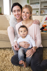 Fototapeta premium Female couple sit together with their son in their home and smile for the camera
