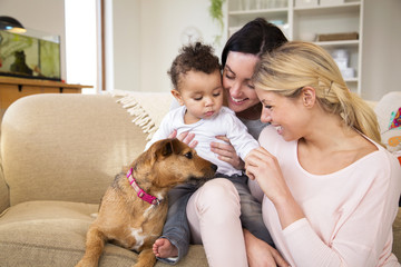 Same sex female couple sitting with their son and dog on the sofa in their home