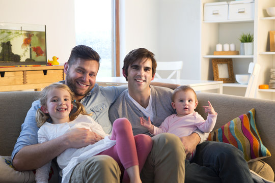 Same sex male couple smiling for the camera with their duaghters at home.