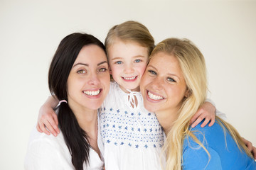 Same sex female couple posing with their daughter in front of a plain background