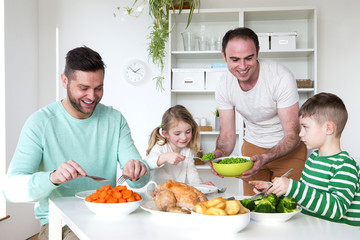 Same sex male couple having dinner with their son and daughter in their home.
