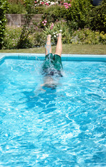 feet of young boy jumping into the pool in front of green plants