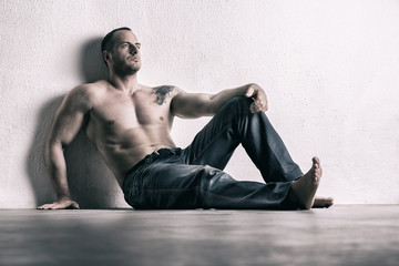 Man posing shirtless, leaning on white wall