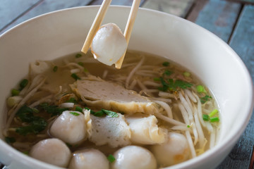 A pair of chopsticks holding a fish ball with a bowl white color