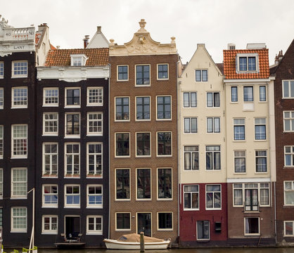 Row of typical crooked building facades lining canal with boat in Amsterdam