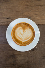 A cup of coffee with heart pattern in a white cup on wooden background