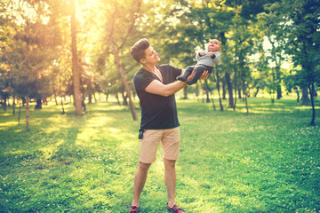 Portrait of father and son having fun in park, father holding baby, infant. Concept of family day in the park with young parents