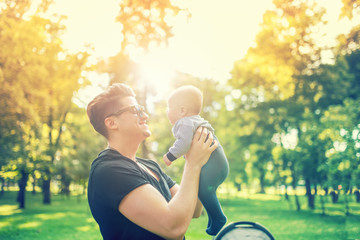 Young father holding delicate newborn infant in arms outdoor in park. Happy parenting concept, father's day and family