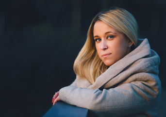 Portrait of a fashionable stylish girl in a coat. Looking and smiling while standing against the fence. Shallow depth of field Outdoors, lifestyle.