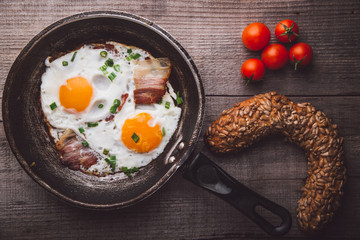 Two fried eggs with bacon and onion, tomato and bread on the side
