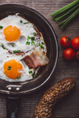 Two fried eggs with bacon and onion, tomato and bread on the side
