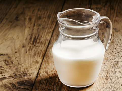 Jug of milk on old wooden table in rustic style, selective focus