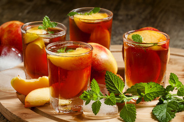Ice Peach Tea with pieces of fruit, ice and mint on a wooden boa