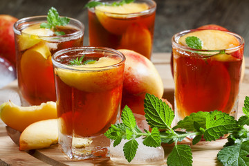 Ice Peach Tea with pieces of fruit, ice and mint on a wooden boa