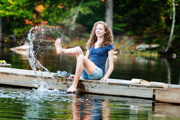 teenage girl sitting on a dock splashing water