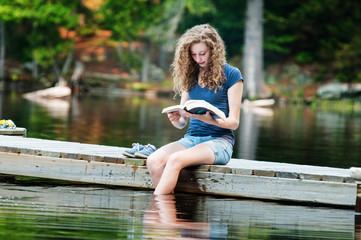 teen girl sitting on a dock reading a book