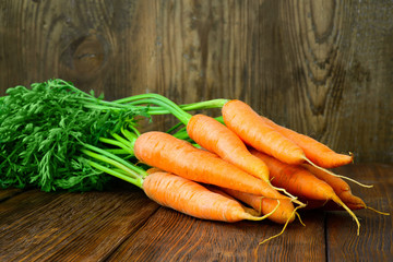 Bunch of fresh carrots with green leaves over wooden background