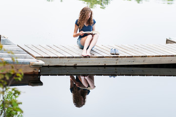 teen girl sitting on a dock reading a book